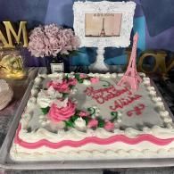 Pink and white Eiffel Tower-themed cake with flowers and “Happy Birthday” decoration