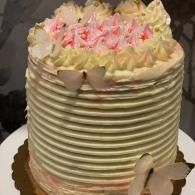 Round frosted cake with pink and cream icing flowers on top and butterfly decorations on the side
