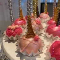 Decorated cake pops with pink and gold icing on sticks, arranged on a white tray