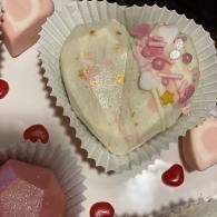 Heart-shaped white candy in a paper cup, surrounded by pink and red heart-shaped candies.