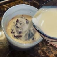 Bowl of cookie dough with chocolate chips as batter is being poured in from a measuring cup