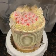 Round cream-frosted cake with pink sprinkles on a white cake stand