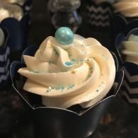 White frosted cupcake with blue sprinkles and a blue candy topper in a black wrapper