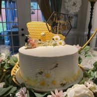 White cake with yellow and white flowers, honeycomb topper, and gold decor on a floral table centerpiece