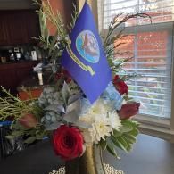 Floral arrangement with red, white, and green flowers and a blue flag on a table by a window