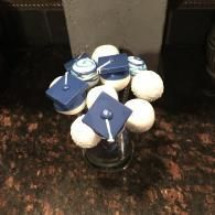 Blue graduation caps with white pompoms arranged on a dark countertop