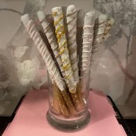 Tall striped and gold-wrapped decorative sticks in a clear glass vase on a pink surface.