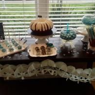 Decorative dessert display on a dark table with cakes and pastries in front of a window with blinds