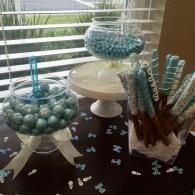 Candy buffet with blue and white treats in glass jars and scattered butterfly confetti on a table
