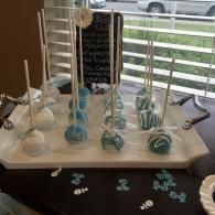 Blue-and-white decorated cake pops on a tray beside a sign on a table by a window