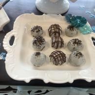 White tray of decorated cake truffles with chocolate drizzle and white icing on a table.