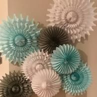 Decorative paper rosettes in white, teal, and black arranged on a beige wall