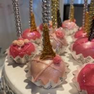 Pink and gold unicorn-themed cake pops with decorative sprinkles and roses on a white tray