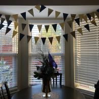 Dining room with black-and-gold bunting, large windows with blinds, and a flower arrangement on a round table