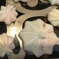 White star-shaped meringue cookies on a dark tray, some lightly browned around the edges.