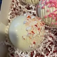 White chocolate truffles in shredded coconut, one topped with red sprinkles and pink drizzle in a box