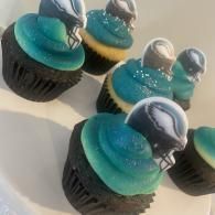 Blue and black frosted cupcakes with white drizzled toppers on a light surface