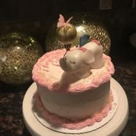 Pink frosted cake with a white bunny figurine and small green bunny topper on a dark countertop