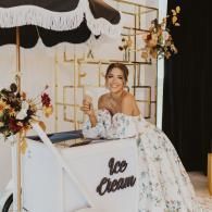 Woman smiling at a white dessert table with floral decor and wedding-style backdrop