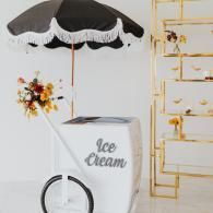 Ice cream cart with black-and-white umbrella and gold dessert stand, decorated with flowers