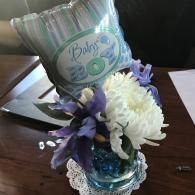 Baby shower centerpiece with white and purple flowers and a “Baby” balloon in a blue vase