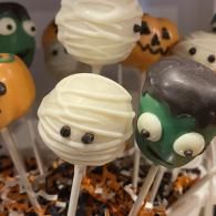 Halloween cake pops decorated as spooky faces with white, green, and orange icing on sticks