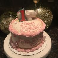 Pink birthday cake with a number 1 topper and “Happy Birthday” icing on a white plate