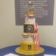 Three-tier decorated cake with gold, white, and red accents on a blue tablecloth.