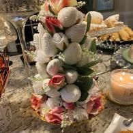Strawberry tower centerpiece with whipped cream, pink flowers, and a candle on a dining table