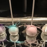 Pastel spherical ornaments hanging above a dark display, in blue, pink, purple, and white.