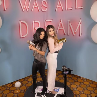 Two people standing back-to-back at a party backdrop with neon “It Was All a Dream” sign