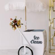 Ice cream cart with white cover, floral bouquet, and black wheel in a bright indoor setting