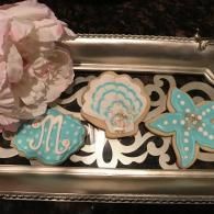 Decorated teal and cream cookies on a silver tray with a white flower arrangement