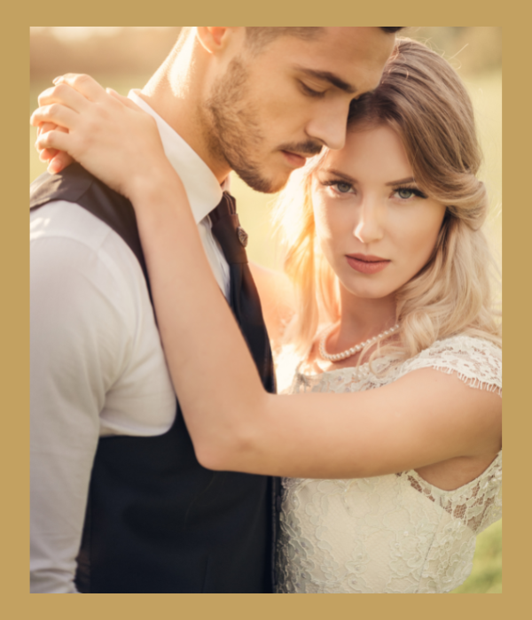 Couple embracing closely in warm sunlight, with the woman in a lace dress and the man in a vest.