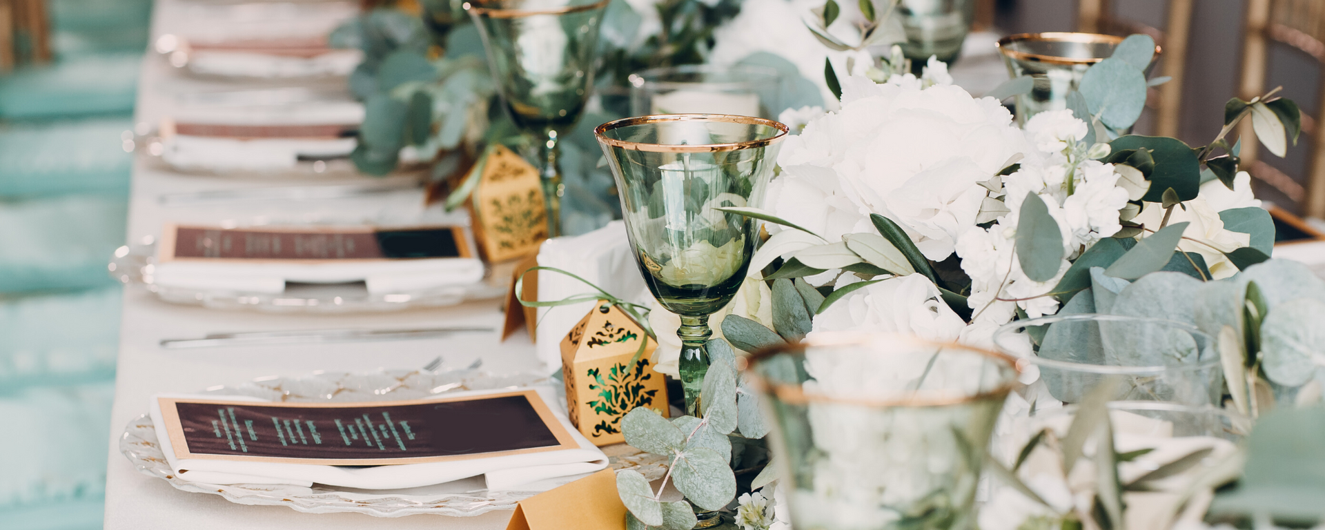 Elegant dining table set with white flowers, green glassware, and place cards on a pastel tablecloth