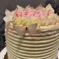 White frosted cake with pink flowers, butterfly decorations, and ribbed sides
