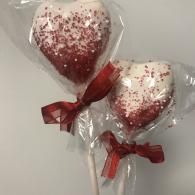 Two heart-shaped lollipops wrapped in clear plastic with red bows and pink sprinkles