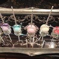 Five pastel-colored treat pops on sticks arranged in a decorative silver holder.