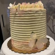 Tall white frosted cake with pastel flowers on a gold board