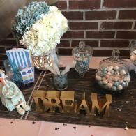 Decorative table display with flowers, jars, candy bowls, and a gold “DREAM” sign against a brick wall