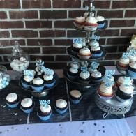 Cupcake display on black and silver stands against a brick wall, with white tablecloth and confetti.