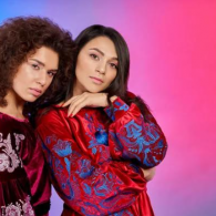 Two people posing against a pink backdrop, wearing red patterned outfits.