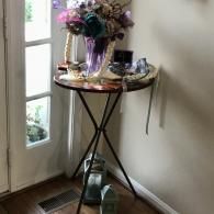 Small round table by a window with flowers, candles, and decor in a hallway corner