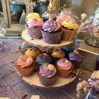 Tiered stand with colorful swirled cupcakes on a dessert table, decorated with purple, pink, and yellow frosting