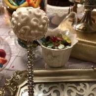 Decorative pearl-topped beaded wand on a silver tray beside assorted sweets in a formal table setting