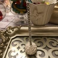 White seashell pendant on a silver chain hanging over an ornate silver tray with a cream vase in the background