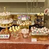 Assorted pastel bath bombs displayed on tiered stands and trays at a decorated table.