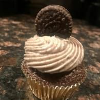 Chocolate cupcake with swirled frosting and a chocolate cookie topper on a dark countertop