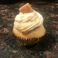 Vanilla cupcake with swirled frosting and a caramel square on top in a foil wrapper
