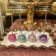 Four pastel crystal balls on silver stands arranged on a tray with a gold lamp in the background